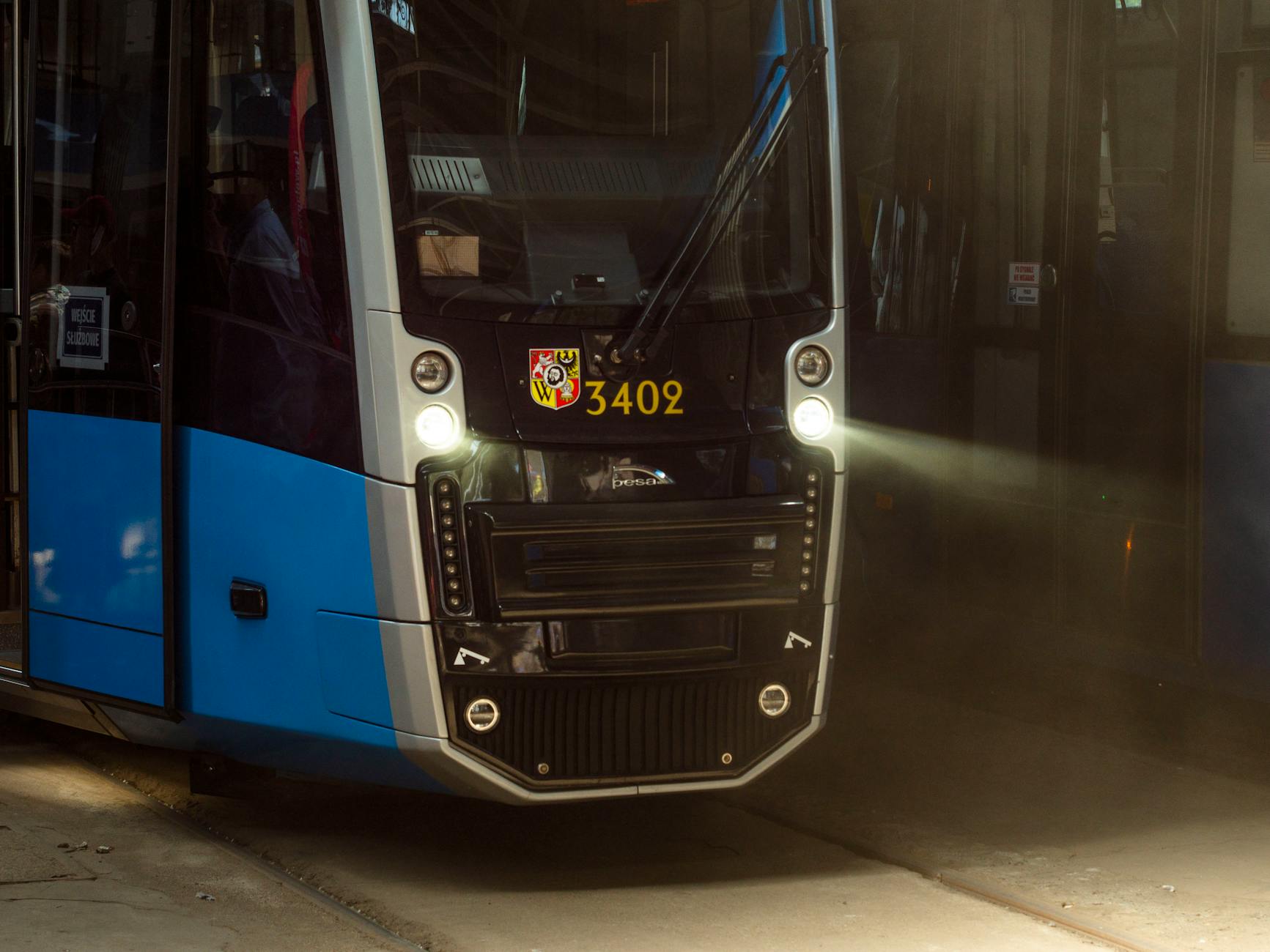 כמה מרוויח נהג רכבת קלה - A modern blue tram with headlights on, captured in an urban setting during the day.