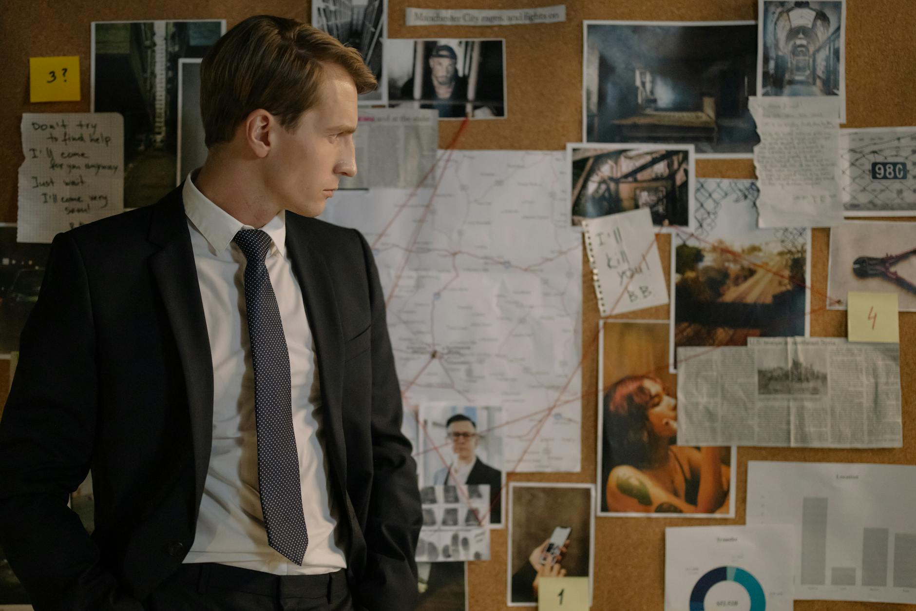 כמה מרוויח חוקר משטרה - Detective in suit examining evidence on cork board during investigation process.