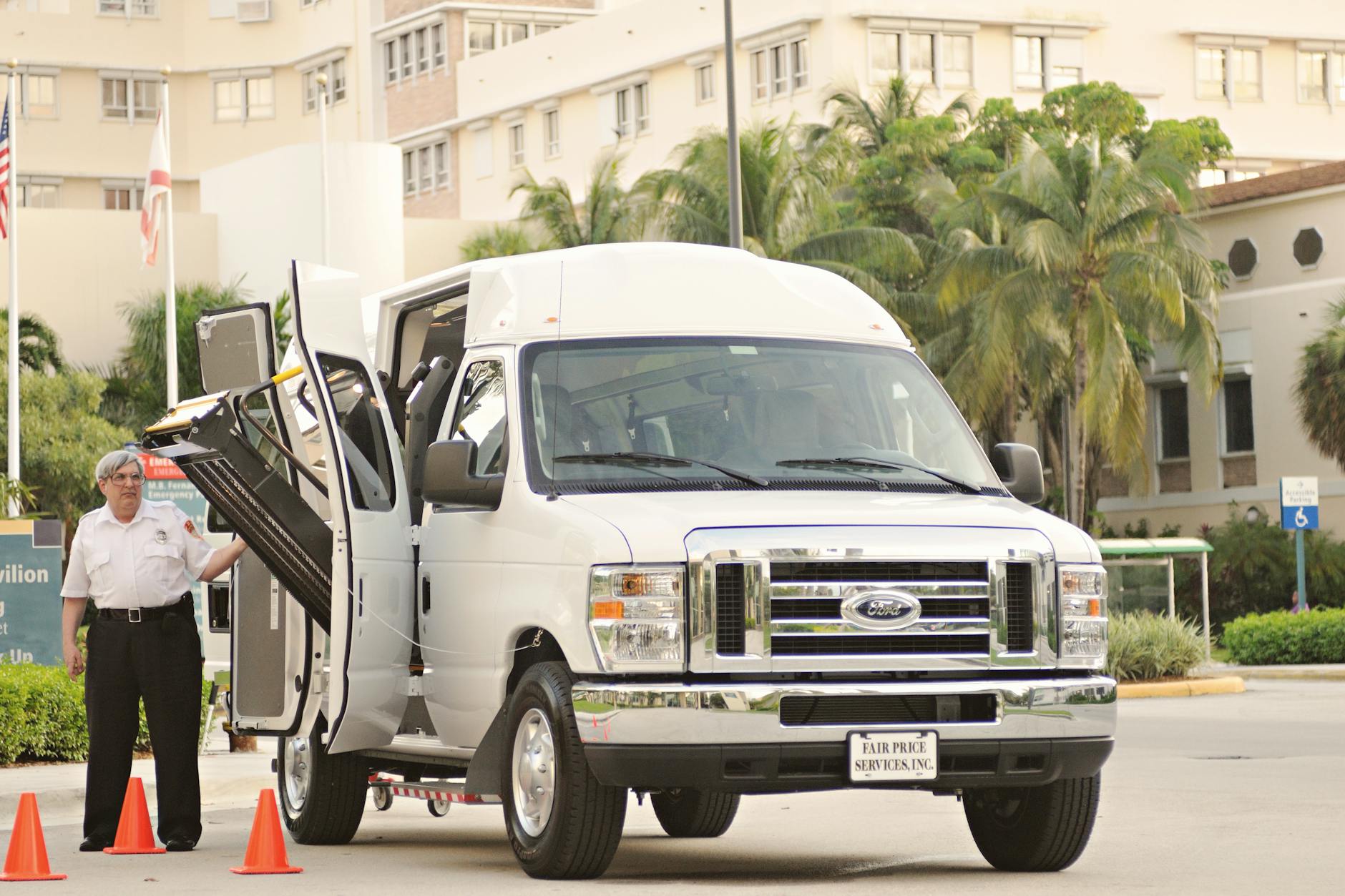כמה מרוויח נהג הסעות - White passenger van with a deployed lift, parked near modern urban buildings.