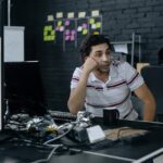 פיטורים בהייטק 2026: Wix, Meta, Intuit. למה זה קורה ואיך להתגונן עובד הייטק יושב במשרד מול מסך וחושב, על רקע קיר לבנים שחור עם פתקיות צהובות וירוקות